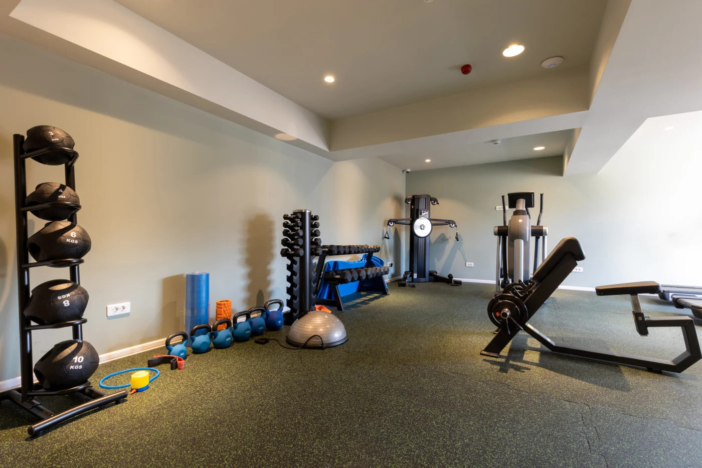 Basement remodeled into an exercise room with dark carpet on the floor and recessed lighting
