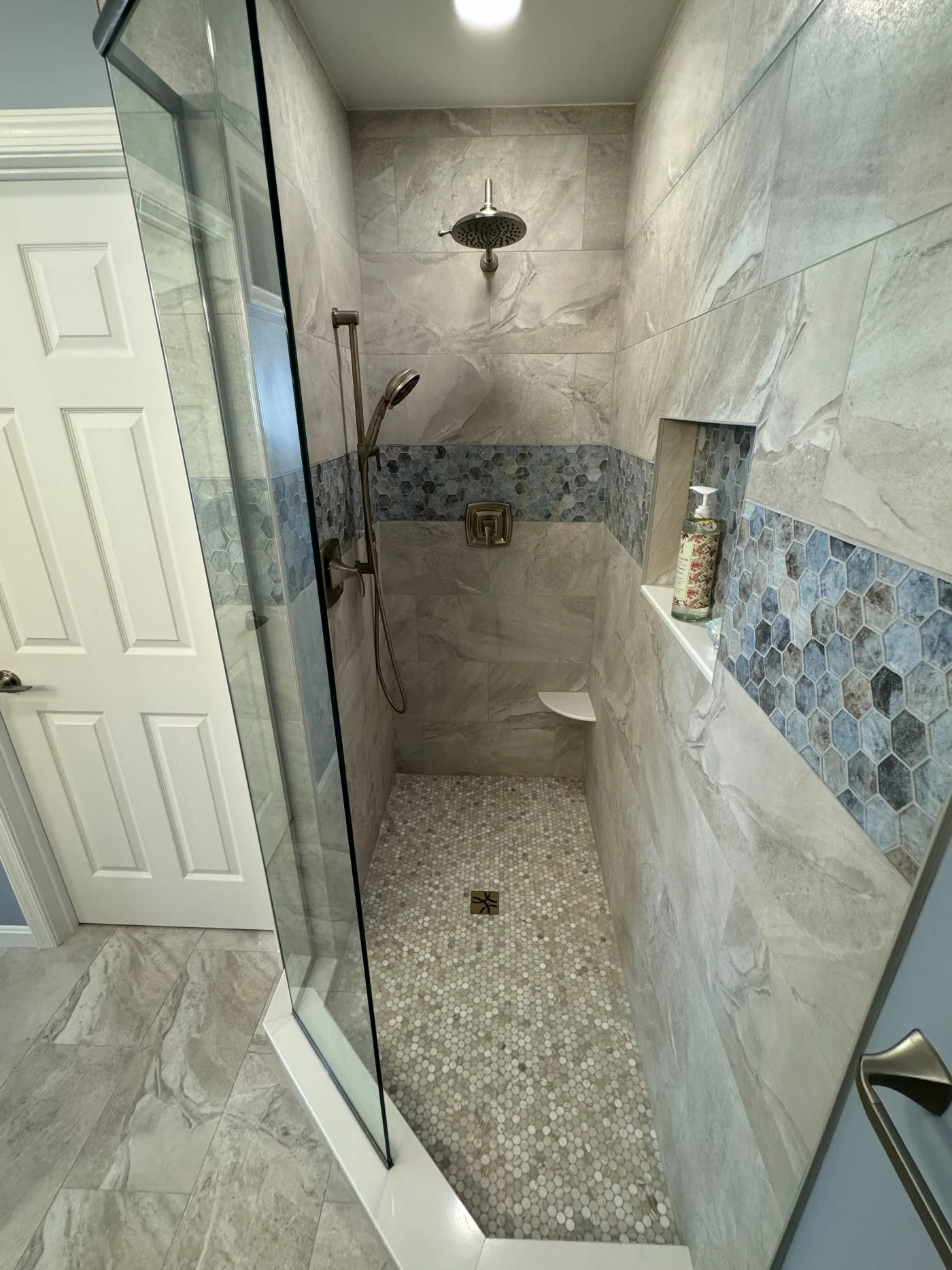 Walk-in shower with an overhead shower head, removable shower head, seat, and built-in shelf