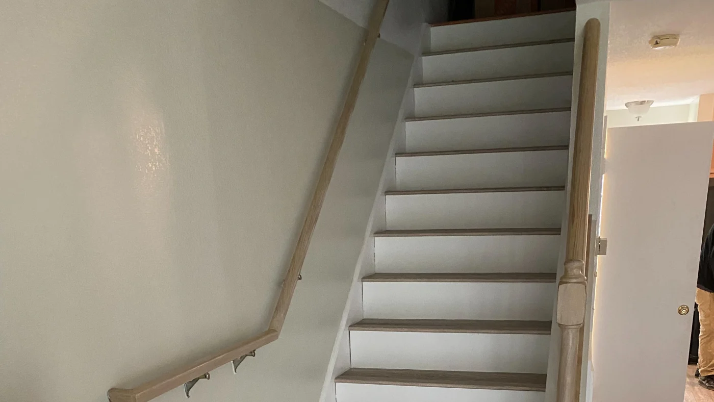 Close up of a staircase with white steps with wooden tops and wooden bannisters.