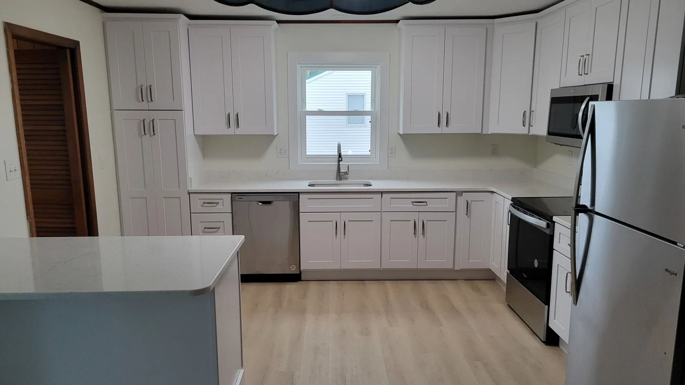 Best Kitchen Remodels In Georgetown, DE | Mast Contracting A newly remodeled kitchen with white cabinetry, wood-grain laminate flooring, and sleek marble countertops with a window over the sink.