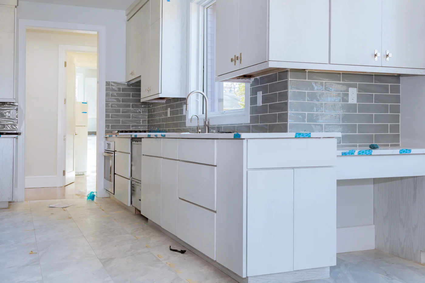 A kitchen in the process of being remodeled with white cabinets and gray subway tile installed as the backsplash.