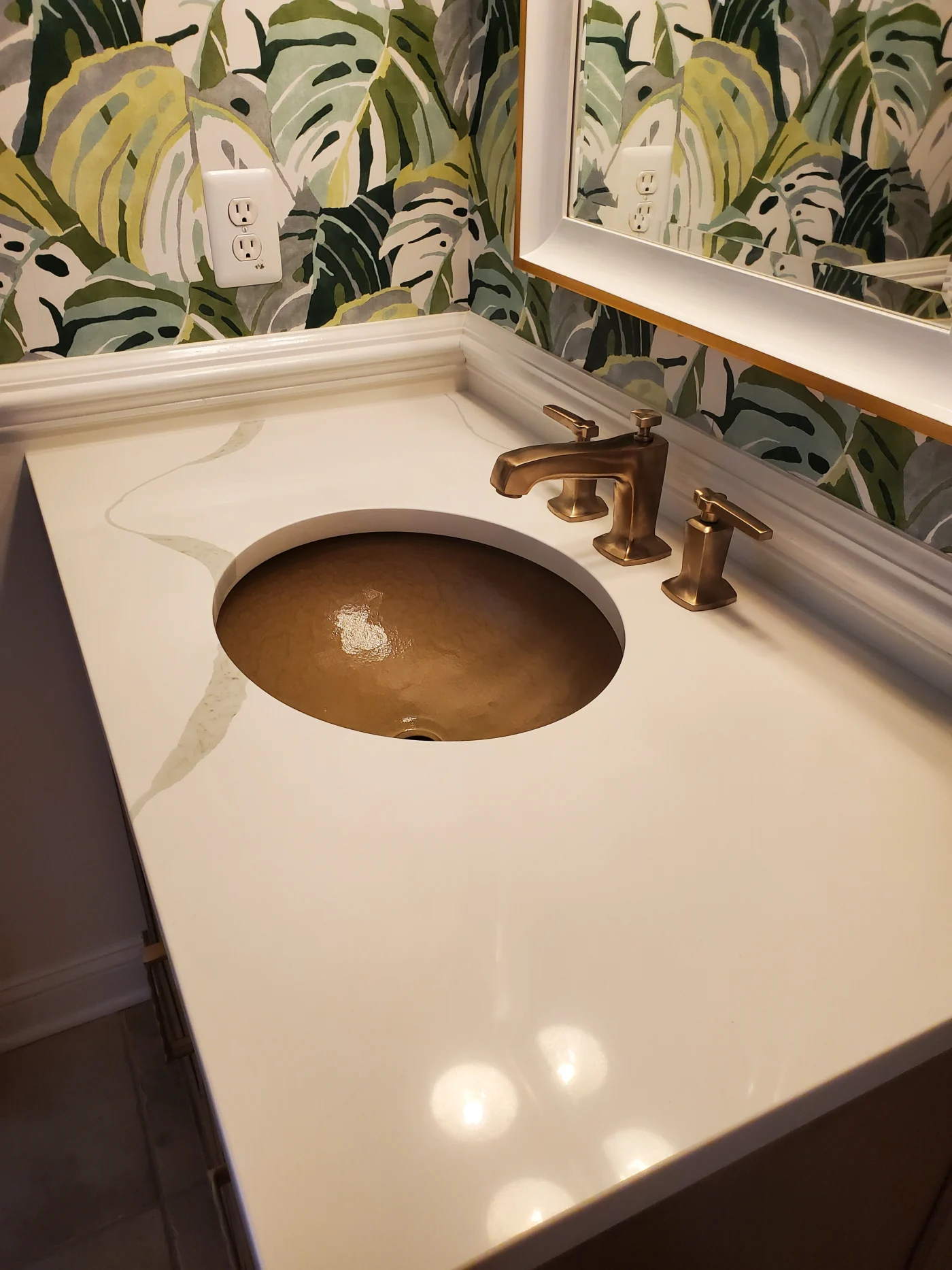 Bathroom vanity with a white countertop and round bronze sink, featuring brushed bronze faucet fixtures.