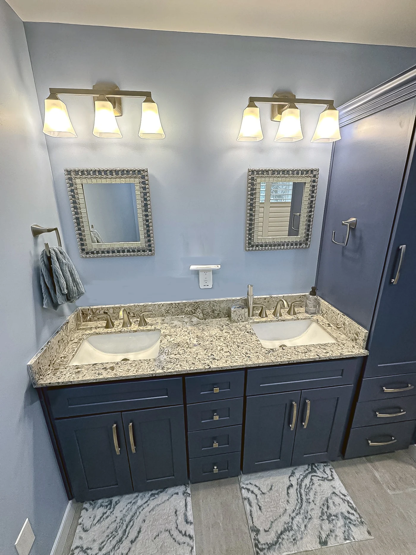 A remodeled bathroom featuring a double-sink vanity with navy cabinets, granite countertops, brushed-nickel faucets, framed mirrors, and modern vanity lights.