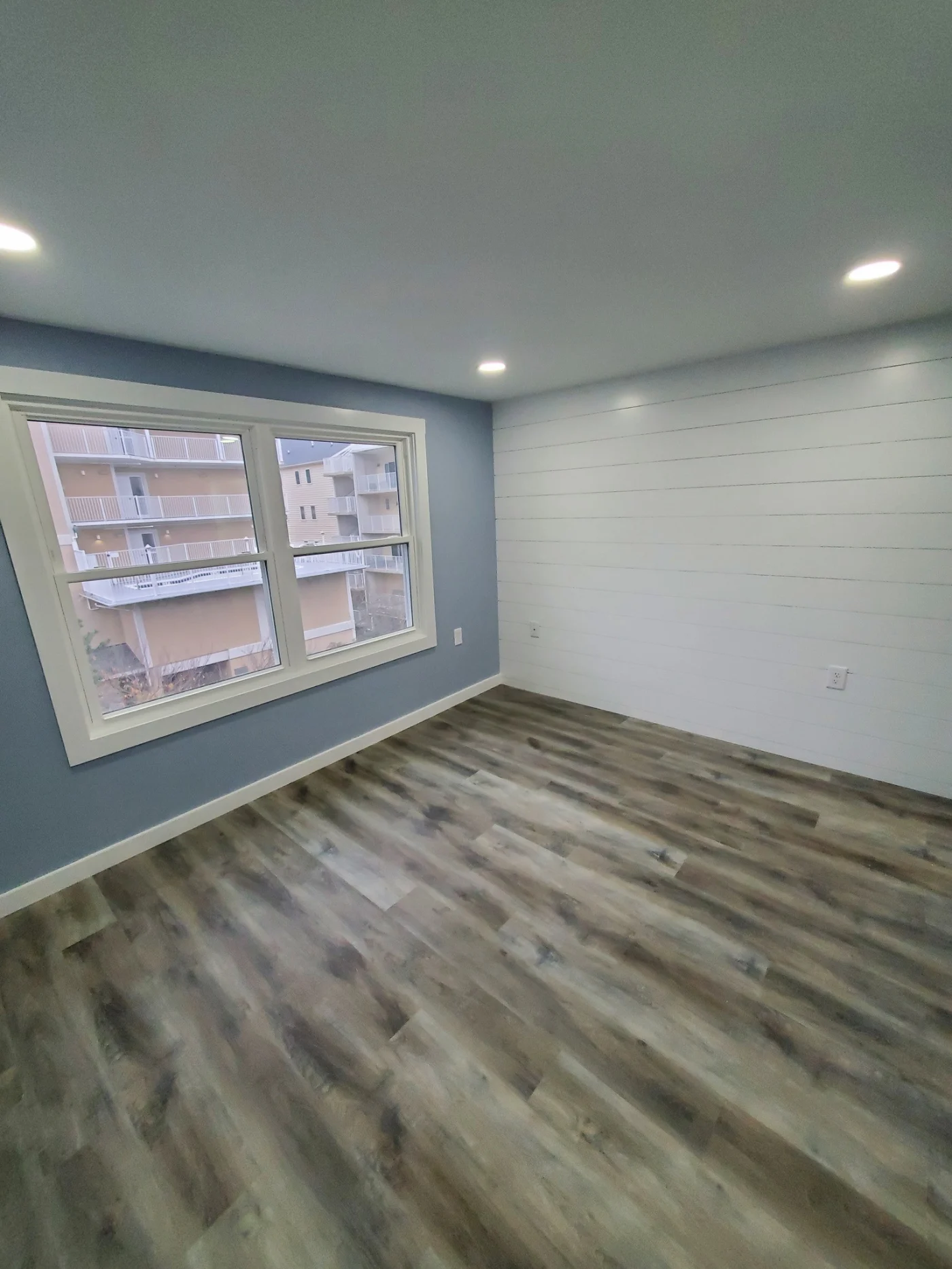 Gorgeous Interior Remodel | Dagsboro, DE | Mast Contracting Bright, newly remodeled bedroom with gray wood-look flooring, soft blue walls, a white shiplap accent wall, and recessed ceiling lights.