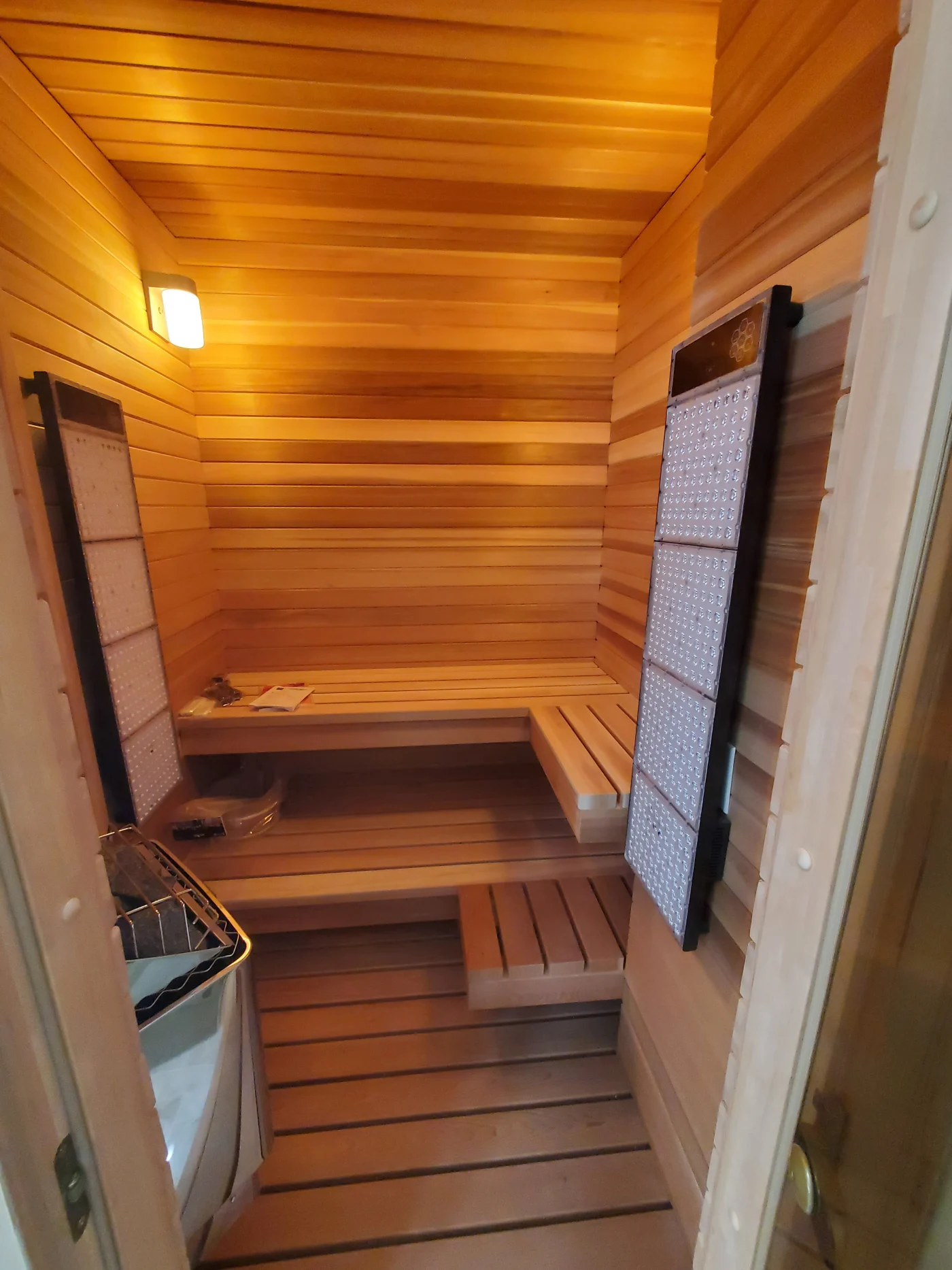 Warm cedar-lined home sauna with tiered wooden benches, wall-mounted heater, and soft overhead light creating a cozy, spa-like interior