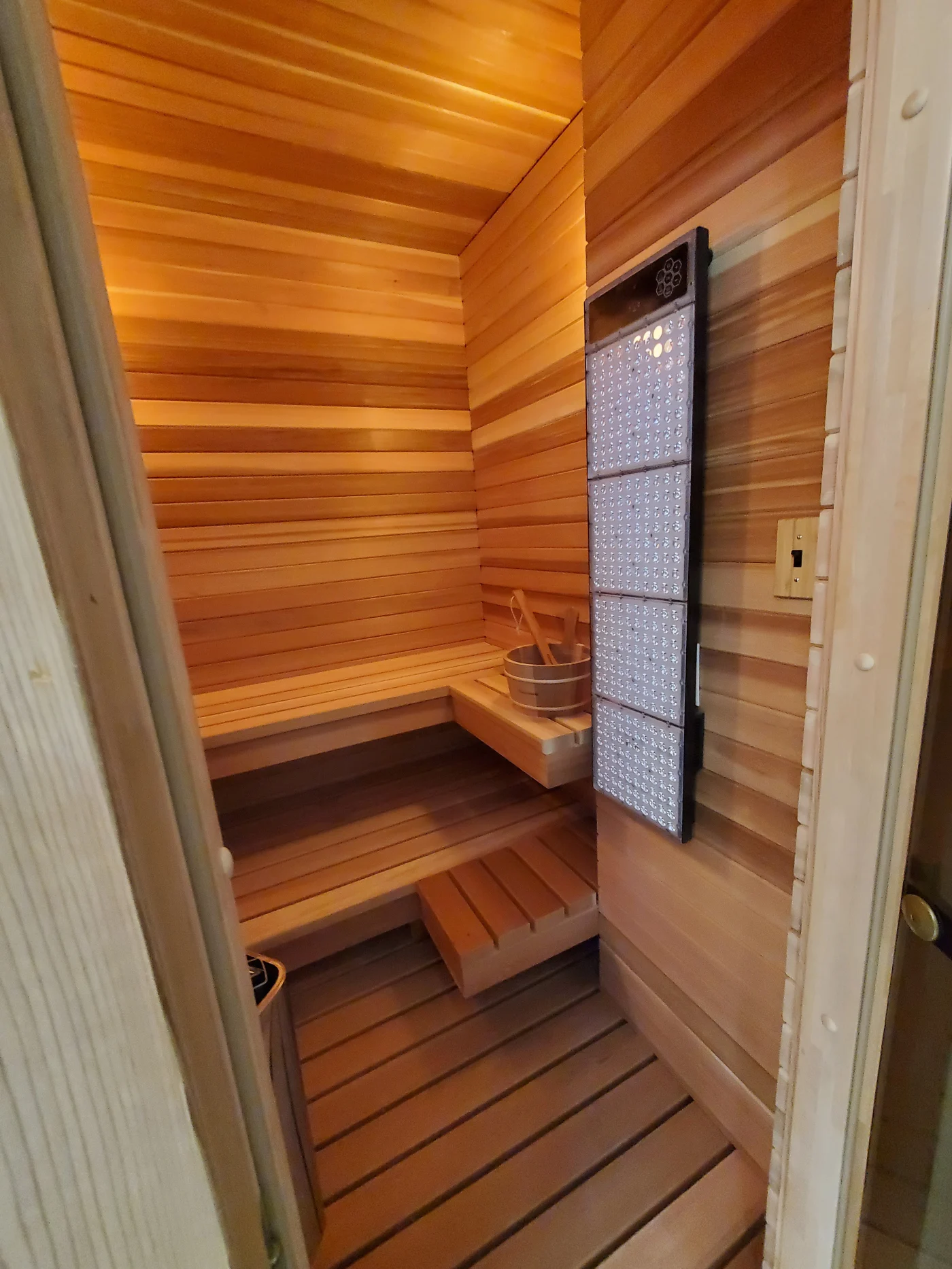 Gorgeous Interior Remodel | Ocean View, DE | Mast Contracting Compact cedar sauna with tiered wood benches, slatted floor, corner bucket and ladle, and a mounted heat panel.