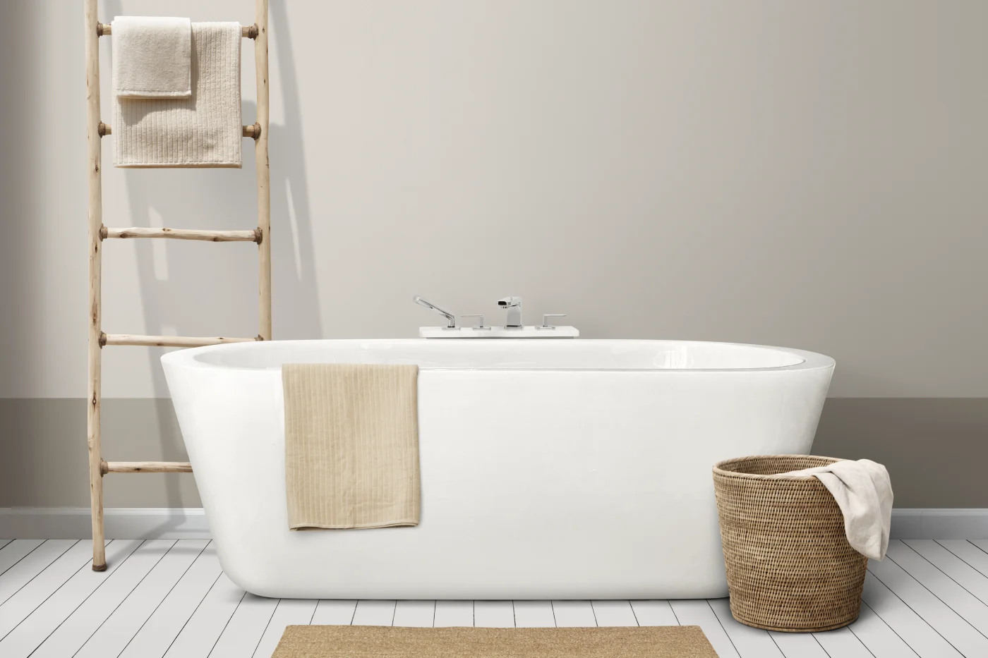 Subtle Full Bathroom Remodel Ocean View, DE | Mast Contracting In the center of the image, a deep, freestanding white bathtub sits on a white tile floor in front of a light colored wall. To the left of the tub, a decorative wooden ladder has cream colored towels hanging from it. There is another towel draped over the side of the tub, and another to the right of the tub, hanging over the edge of a wicker basket.