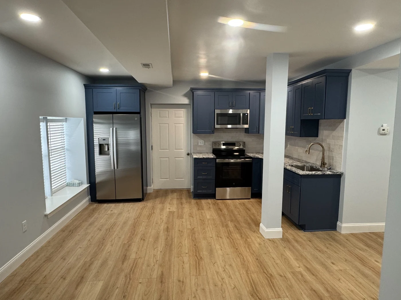 Open remodeled kitchen with navy cabinets, stainless appliances, granite counters, tile backsplash, wood-look flooring, and recessed lights.