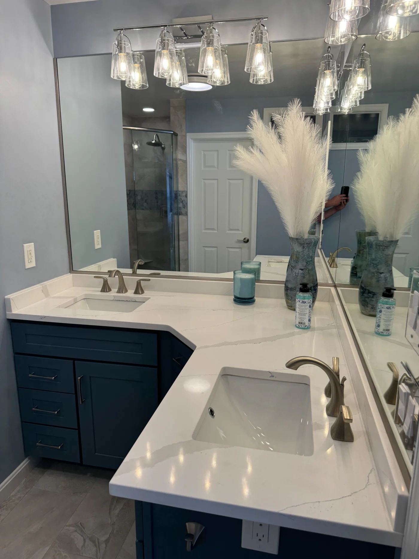 Impressive Full Bathroom Remodel | Rehoboth Beach, DE | Mast Contracting Remodeled bathroom with navy double vanity, white quartz counters, twin sinks, wall mirrors, glass pendant lights, and a walk-in shower.