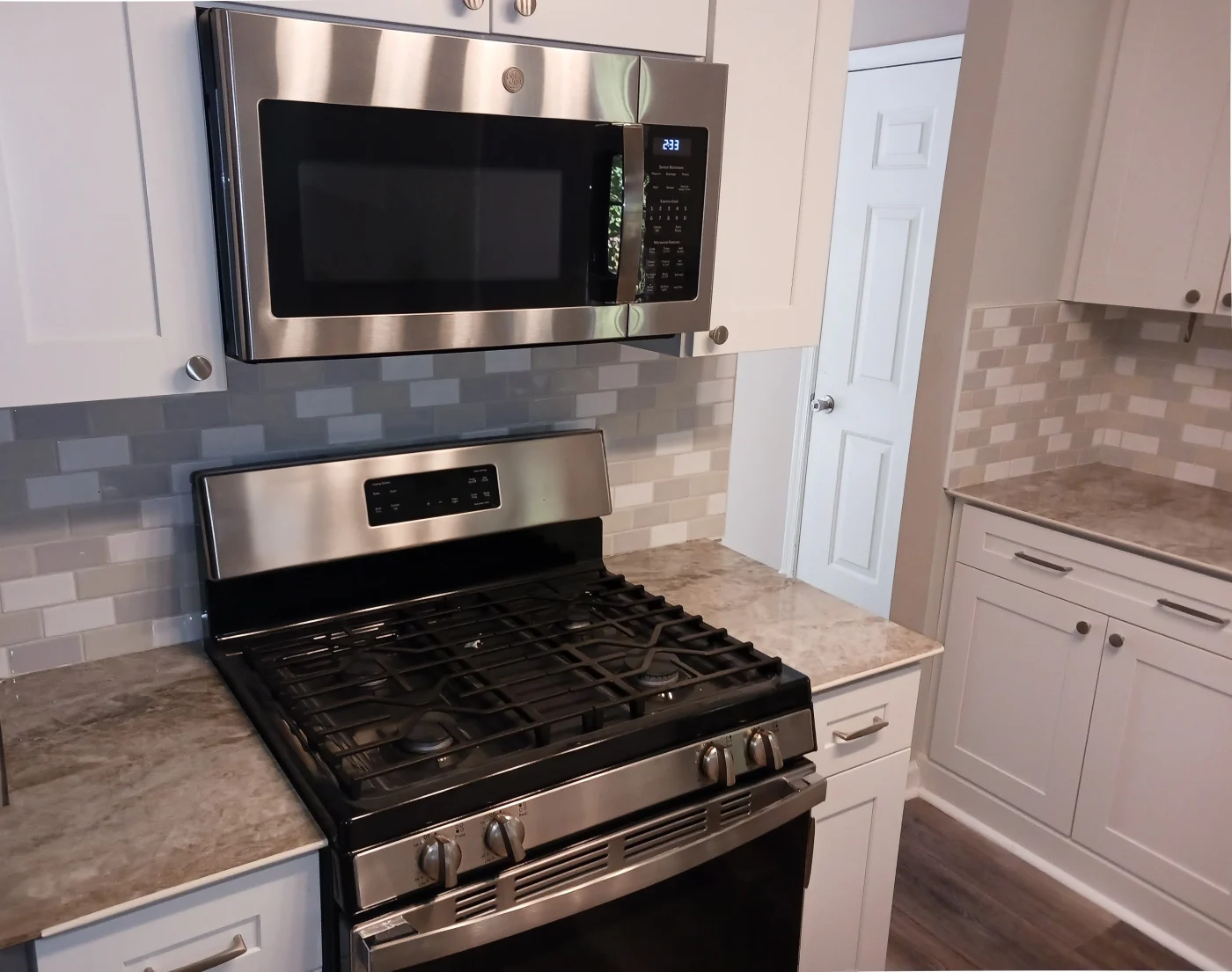 This bright space features white Shaker cabinets, a subway-tile backsplash, marbled countertops, and stainless steel appliances, the result of a successful kitchen remodeling project.